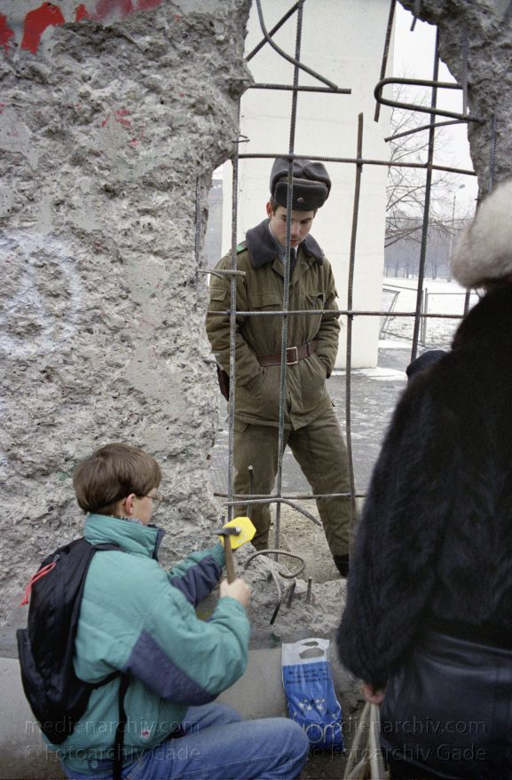 Lücke in der Berliner Mauer.
7. 1. 1990. Berlin. Mitte. Berliner Mauer beim Reichstag. DDR-Grenze zwischen Tiergarten und Mitte. Ein DDR Grenzposten und Besucher betrachten sich durch eine Lücke in der Mauer. Mauerspecht
Schlüsselwörter: Berlin;berlin wall;Berliner Mauer;DDR;GDR;Germany;Grenze;Grenzposten;Mauerspecht;Mitte;1990;Ostberlin