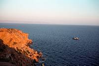 1968. Griechenland. Kap Sounion. Felsen von Kap Sounion in der Abendsonne davor langes Schiff mit kleinem Segel