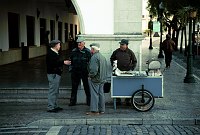 November 2000. <br>Portugal. Tavira.  Der Maronenröster verkauft heisse Kastanien. Männer an der Straße. Karren.